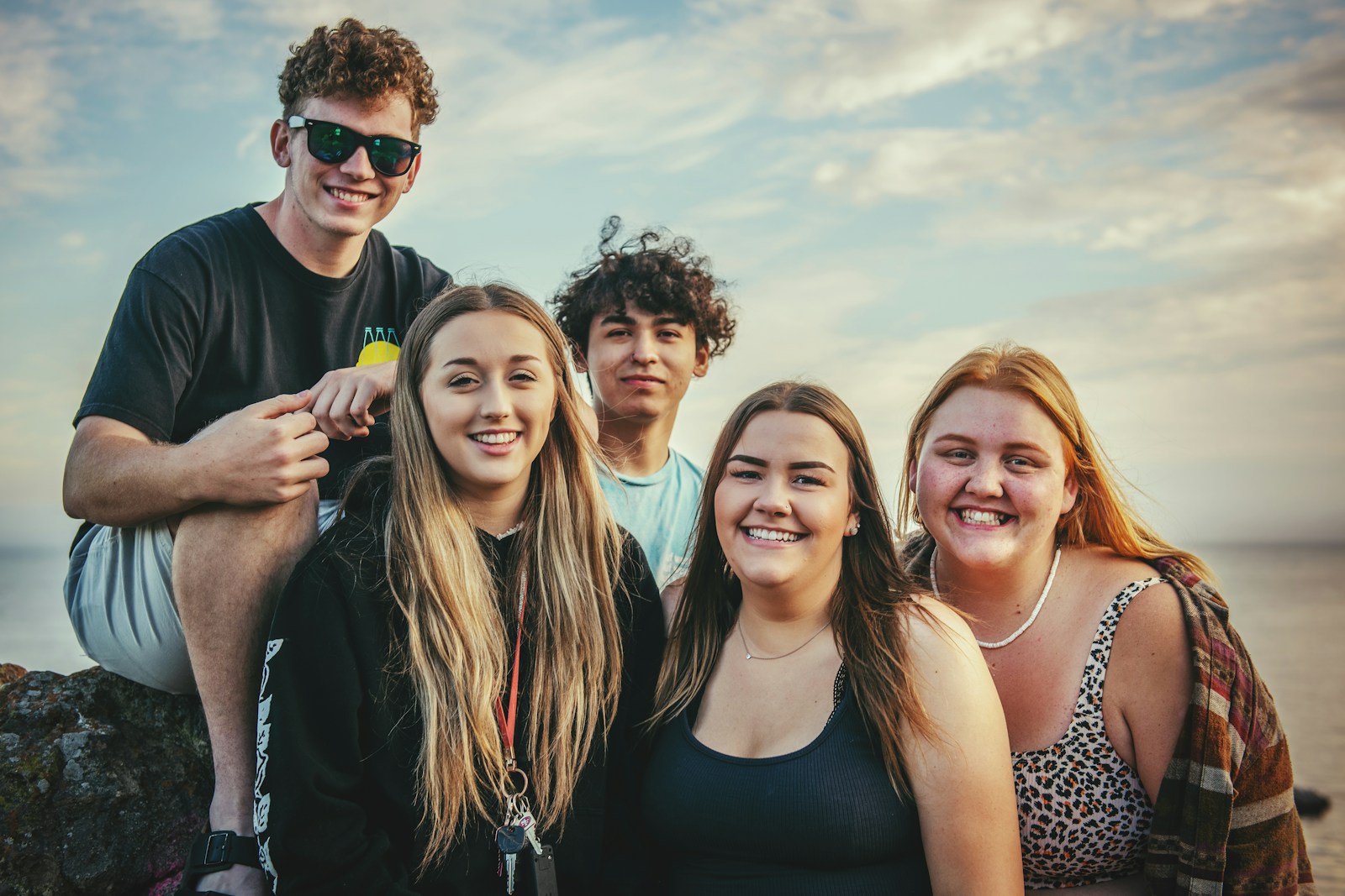 A group of five smiling teenagers outdoors at sunset